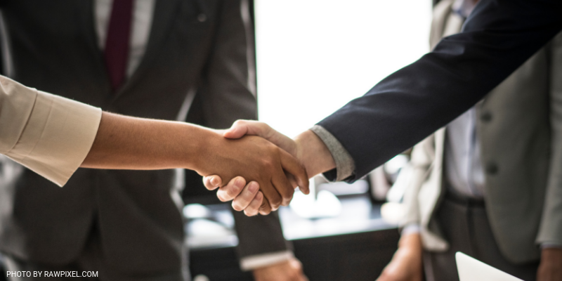 two people shaking hands in an office. Only their arms and hands are visible.