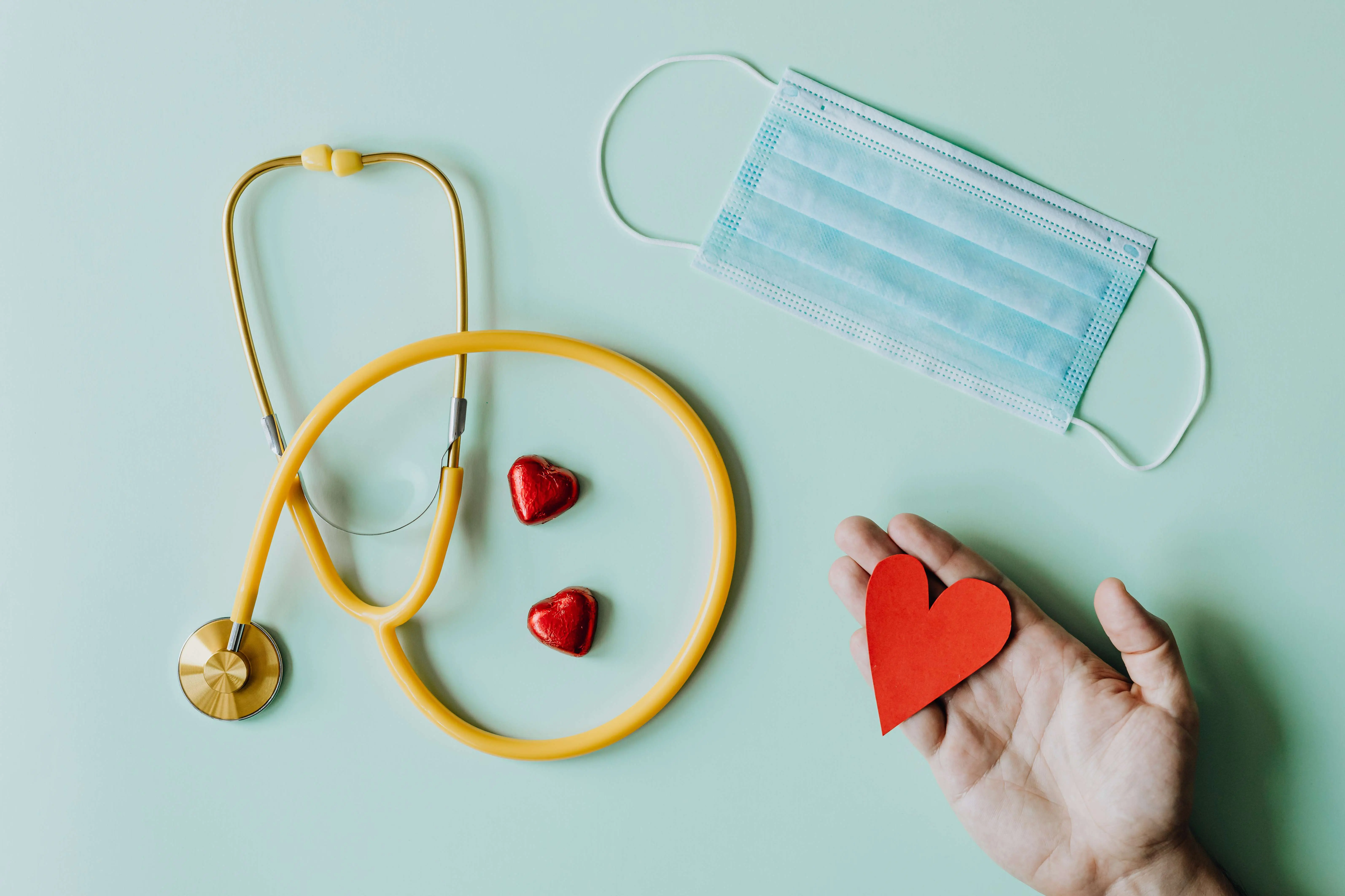 Photo of a medical stethoscope on a table with a hand holding paper hearts.