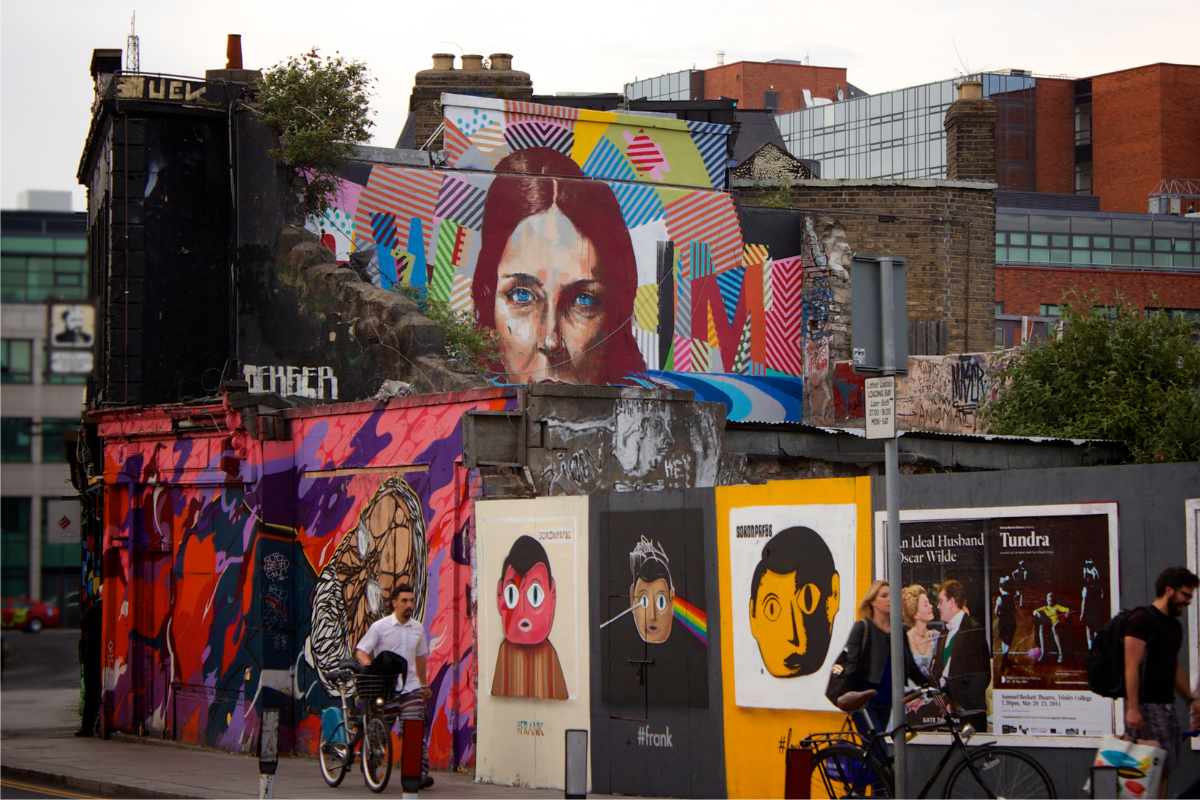 Photograph of sidewalk with construction hoarding feature posters, murals, and artwork in a city