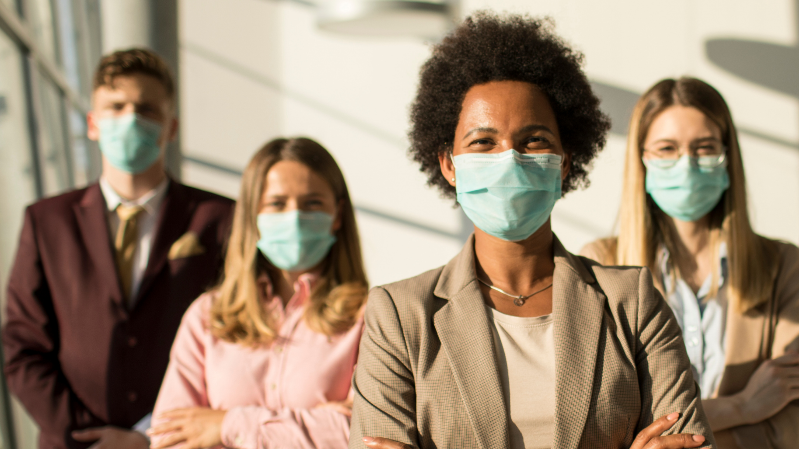 Four people wearing surgical masks standing and facing the camera with arms crossed.
