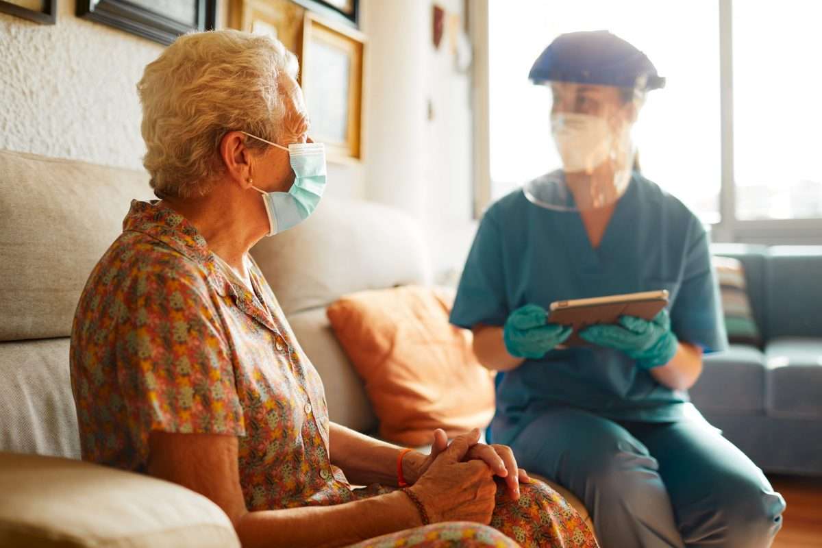 A female doctor visits a senior woman at the nursing home during COVID.